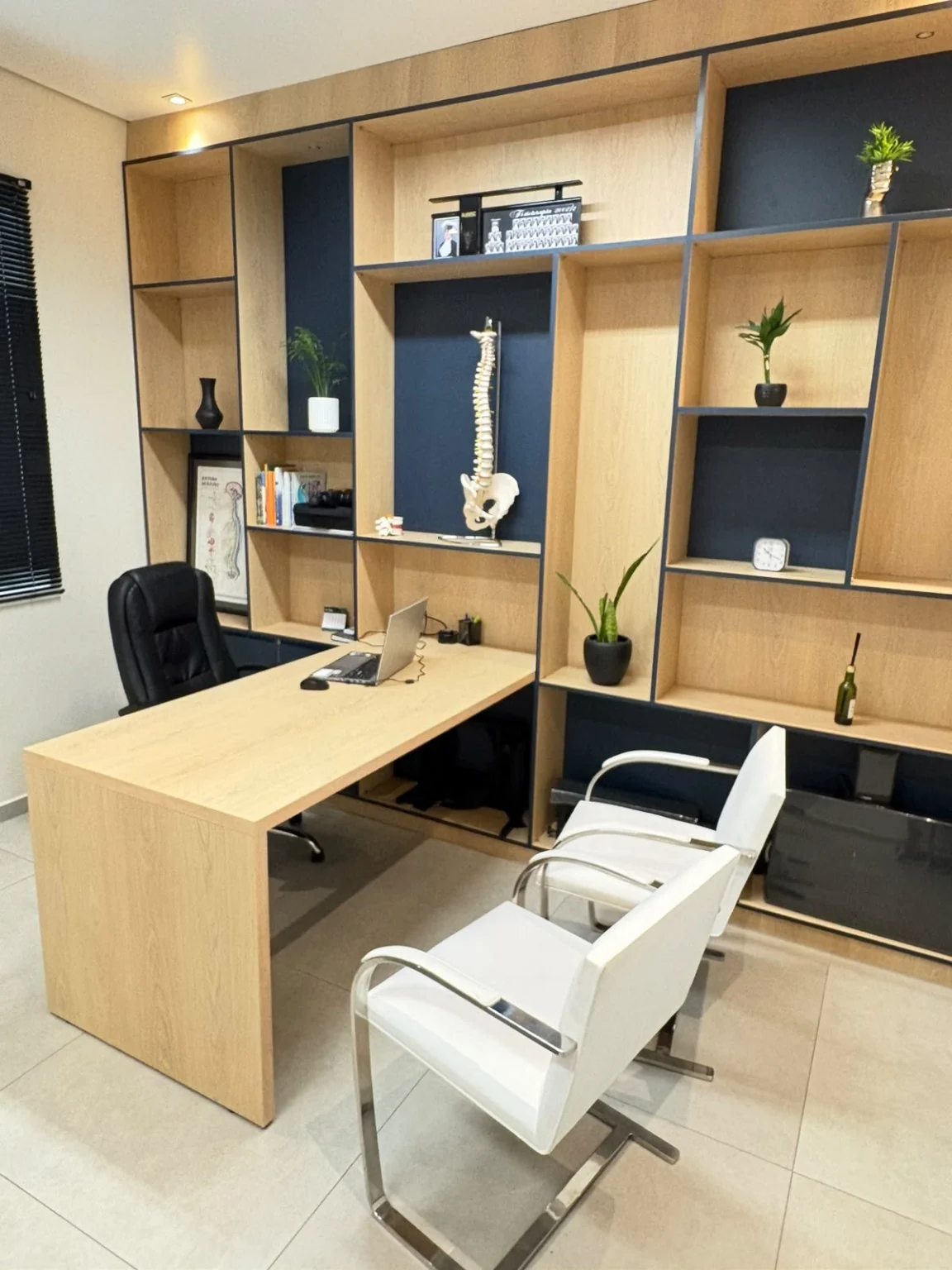Consultório da Posture Clínica da Coluna com mesa de atendimento e estante de madeira